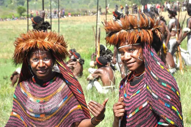 Two young indigenous West Papuan girls standing together wearing traditional Sali clothing made from brown tree bark.