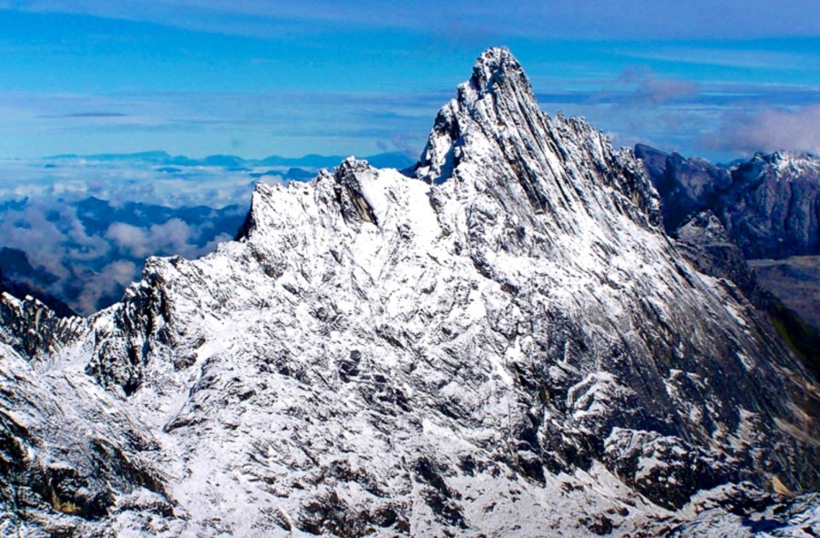 Professional mountaineer climbing the steep, sharp limestone cliff of Carstensz Pyramid, illustrating key Mount Carstensz facts about its extreme technical terrain.