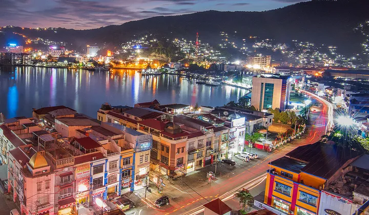 A wide-angle night view of Jayapura City showing thousands of urban lights nestled between the dark mountains and the edge of Humboldt Bay.