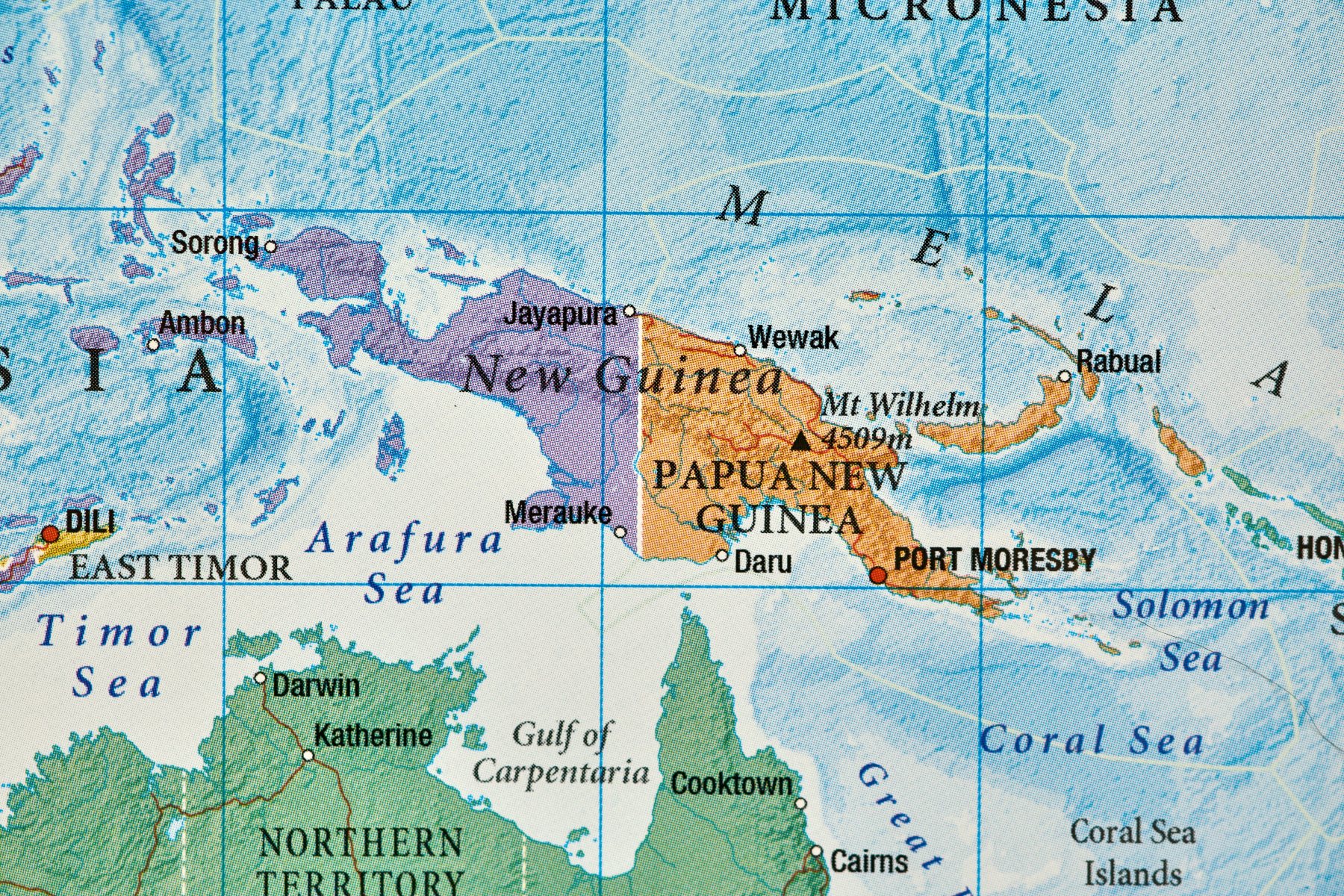 A detailed political and geographical map of Papua Island, showing the division between West Papua (Indonesia) on the western side and Papua New Guinea on the eastern side, with the central mountain range stretching across the island.